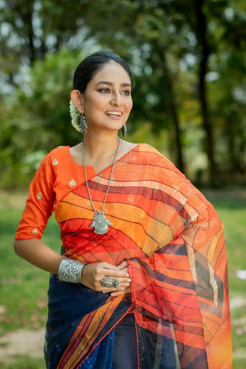 Deep navy blue organza saree with vibrant orange geometric digital print pattern embroidered blouse silver tribal pendant necklace jasmine flower earrings outdoor portrait ethnic contemporary fashion